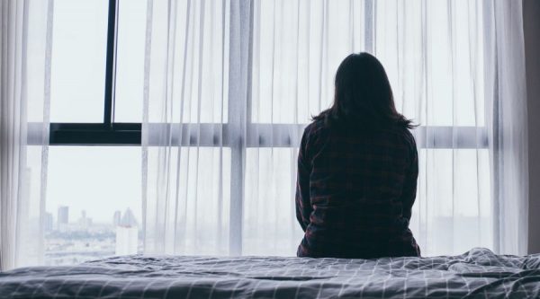 Woman sitting on bed looking out the window with her back to the camera