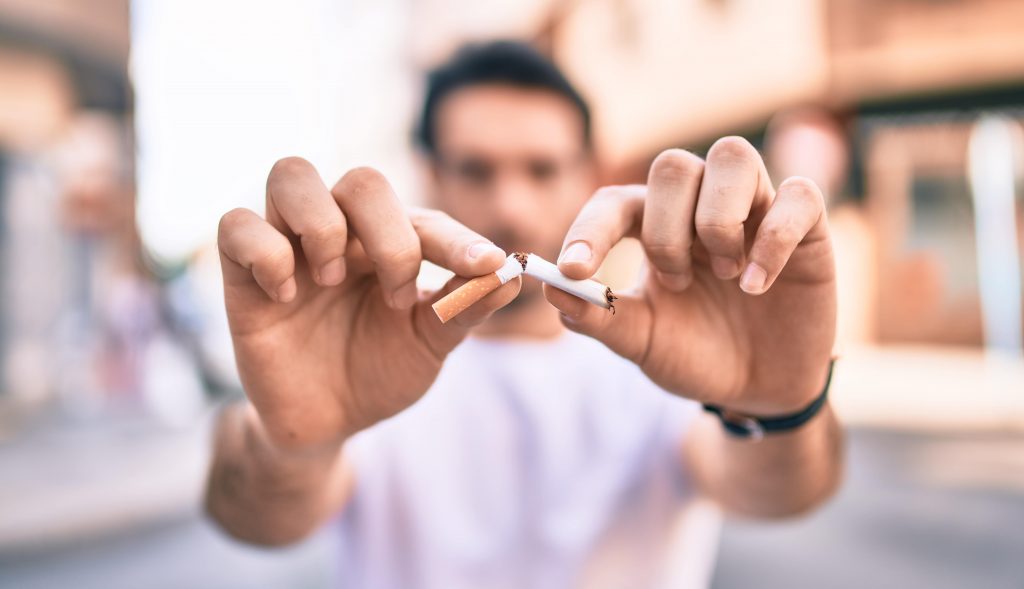 man breaking a cigarette in half with his two hands