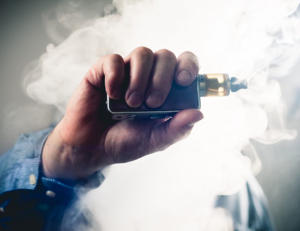 Male hand holding a vape surrounded by smoke