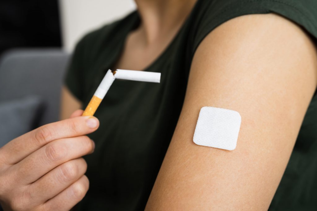 broken cigarette being held next to lady's arm with smoking patch