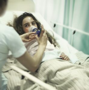 A young woman in a hospital bed wearing breathing apparatus