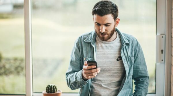 Man using his smartphone while leaning against window sill.