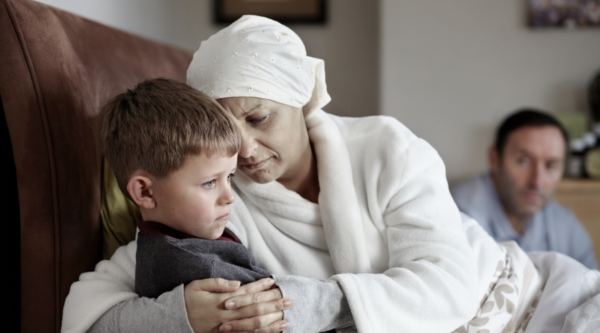 Woman who appears seriously ill sitting on the sofa holding her young son.