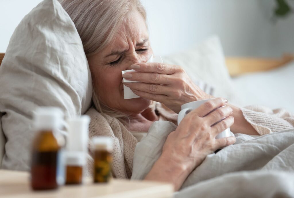 Woman lying in bed holding a tissue next to bottles of medication